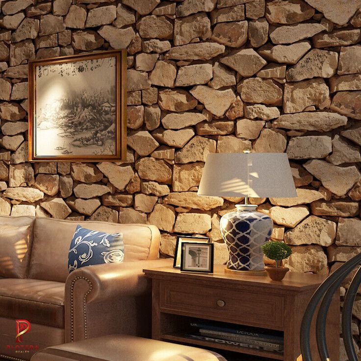 A cozy living room featuring a textured brick and stone wallpaper that mimics a natural rock wall. The space is styled with a tan leather sofa, a wooden side table, and a decorative ceramic lamp.